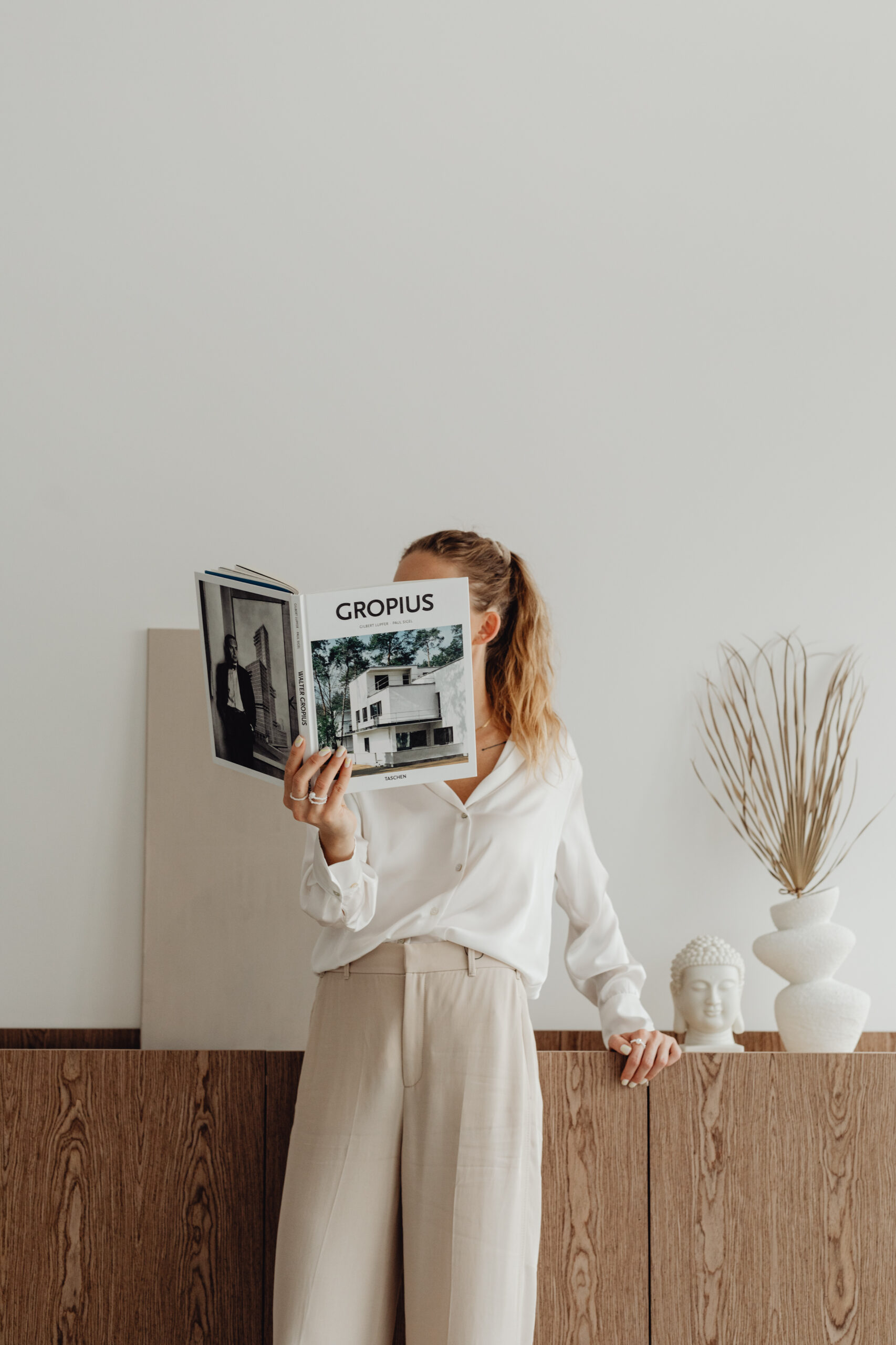 woman with a curly ponytail reading a book and standing against a desk