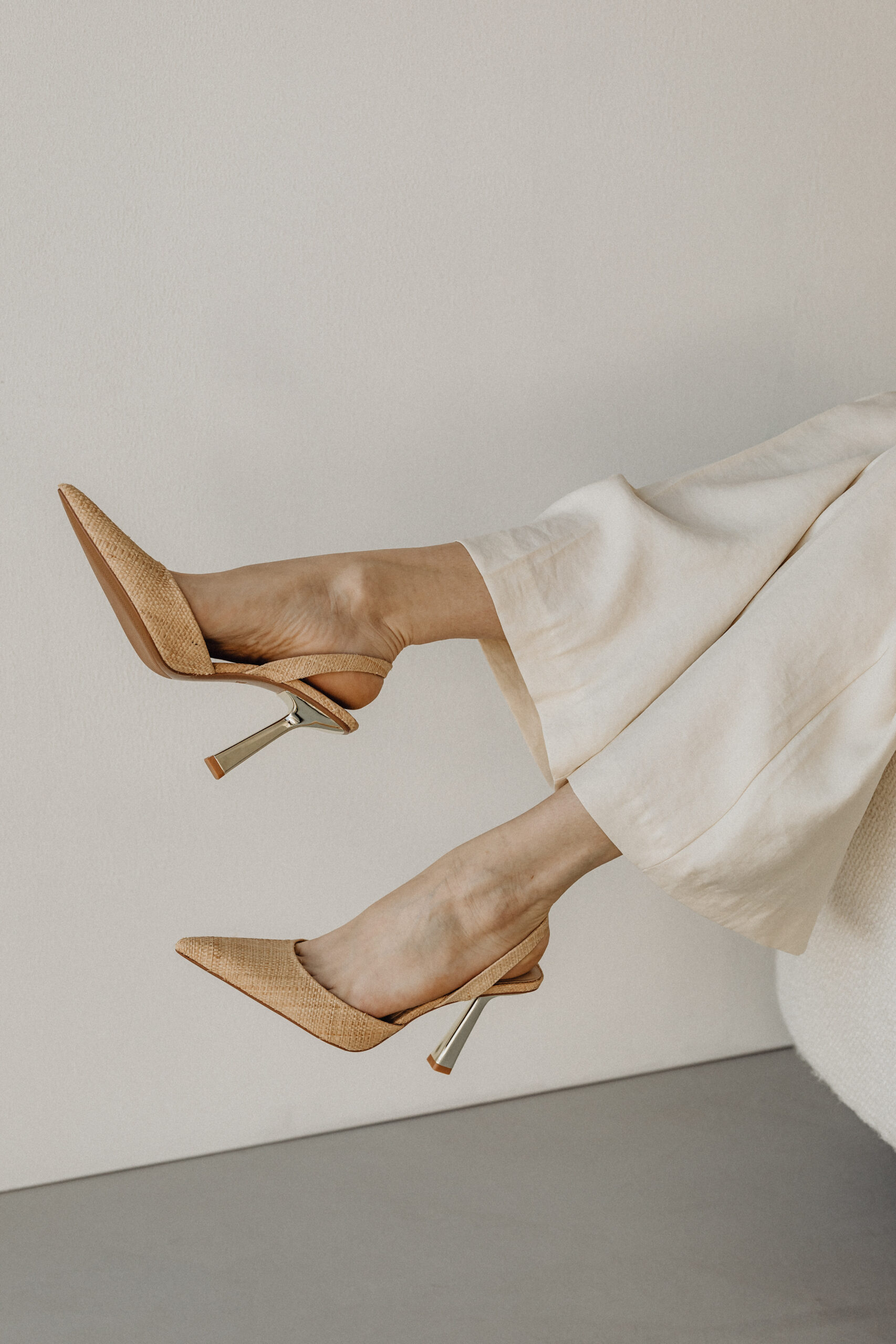 woman in off white palazzo pants and tan pumps on a chair with her feet up