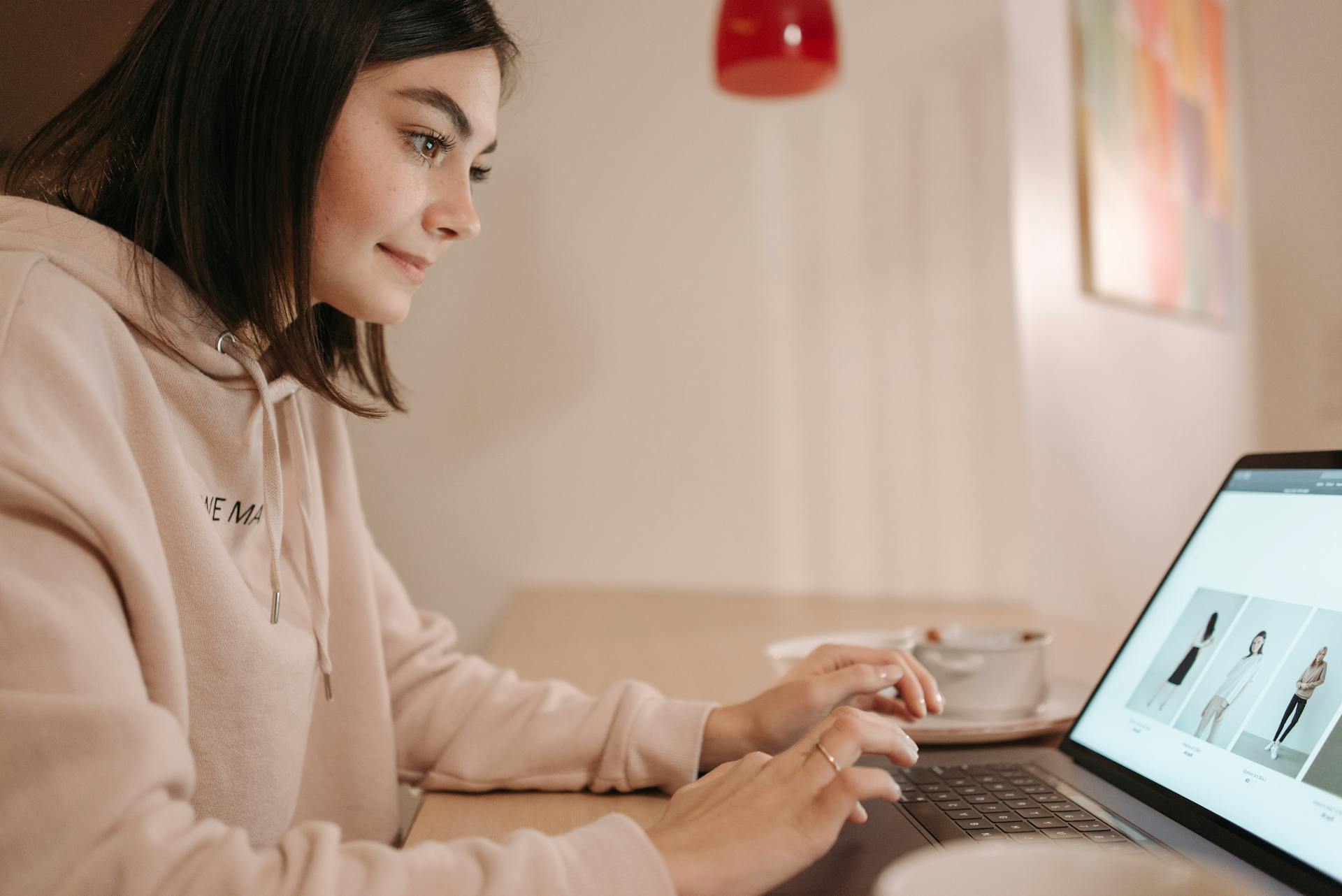 girl in hoodie smiling and typing on a laptop